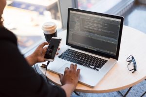 Männerhand mit Handy und Laptop im Hintergrund