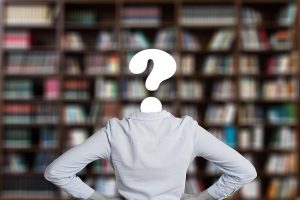 Student mit symbolischen Fragezeichen statt Kopf stehrt vor einer Bücherwand